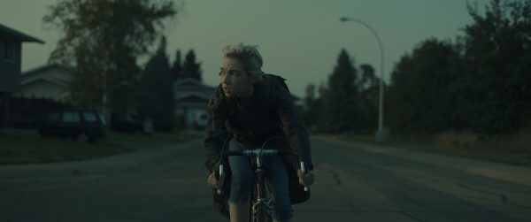 Sarah, the protagonist, riding a bicycle down the street.